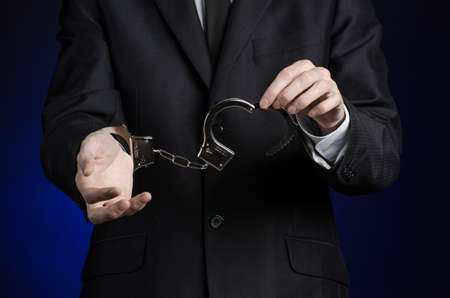 Corruption and bribery theme: businessman in a black suit with handcuffs on his hands on a dark blue background isolatedの写真素材