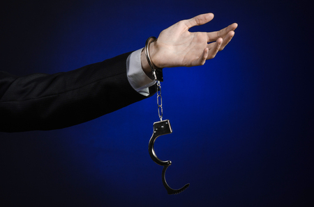 Corruption and bribery theme: businessman in a black suit with handcuffs on his hands on a dark blue background isolatedの写真素材