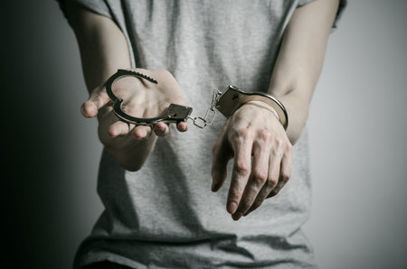 Prison and convicted topic: man with handcuffs on his hands in a gray T-shirt on a gray background,...