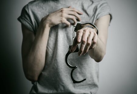 Prison and convicted topic: man with handcuffs on his hands in a gray T-shirt on a gray background, put handcuffs on rapistの写真素材