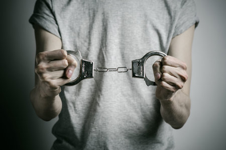 Prison and convicted topic: man with handcuffs on his hands in a gray T-shirt on a gray background,...