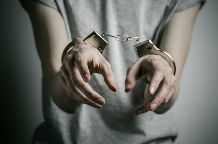Prison and convicted topic: man with handcuffs on his hands in a gray T-shirt on a gray background,...