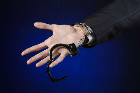 Corruption and bribery theme: businessman in a black suit with handcuffs on his hands on a dark blue background isolatedの写真素材