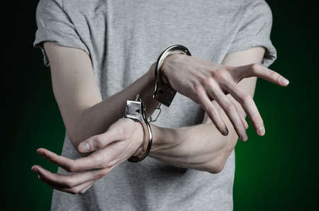 Prison and convicted topic: man with handcuffs on his hands in a gray T-shirt and blue jeans on a dark green background, put handcuffs on the drug dealerの写真素材