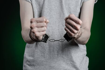 Prison and convicted topic: man with handcuffs on his hands in a gray T-shirt and blue jeans on a dark green background, put handcuffs on the drug dealerの写真素材