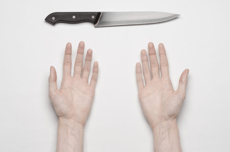 Murder and Halloween theme: A man's hand reaching for a knife, a human hand holding a knife isolated on a gray background from aboveの写真素材