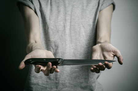 Murder and Halloween theme: a man holding a knife on a gray background studio