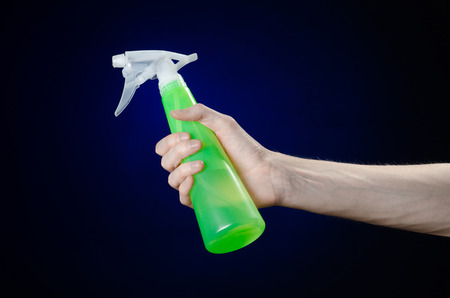 Cleaning the house and cleaner theme: man's hand holding a green spray bottle for cleaning on a dark blue background studioの写真素材