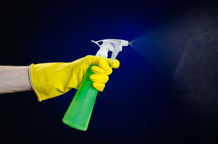 Cleaning the house and cleaner theme: man's hand in a yellow glove holding a green spray bottle for cleaning on a dark blue background studioの写真素材