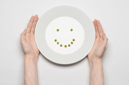 Healthy food theme: hands holding a plate of green peas on a white table top view studioの写真素材