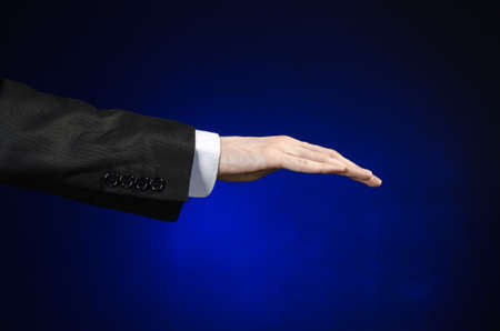 Businessman and gesture topic: a man in a black suit and white shirt showing hand gesture on an isolated dark blue backgroundの写真素材