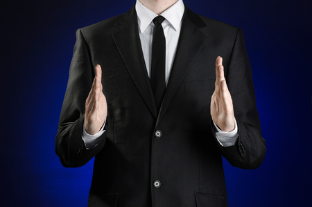 Businessman and gesture topic: a man in a black suit and white shirt showing gestures with hands on a dark blue background in studioの写真素材