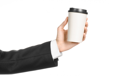 Business lunches coffee theme: businessman in a black suit holding a white blank paper cup of coffee with a brown plastic cap isolated on a white background in the studioの写真素材