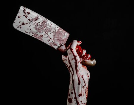 Bloody Halloween theme: bloody hand holding a large bloody kitchen knife on a black background isolatedの写真素材