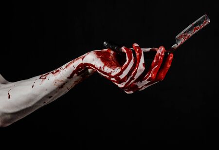 Bloody Halloween theme: bloody hand holds a razor sharp old with a dangerous edge isolated on black backgroundの写真素材
