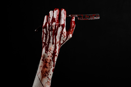 Bloody Halloween theme: bloody hand holds a razor sharp old with a dangerous edge isolated on black backgroundの写真素材