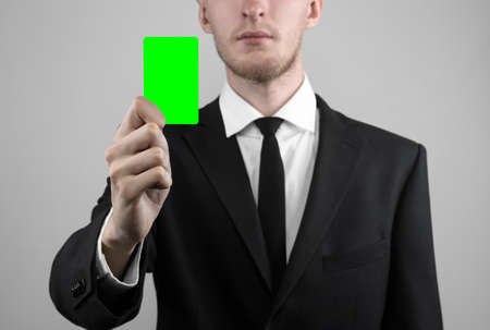 businessman in a black suit and black tie holding a card, a hand holding a card, green card, card is inserted, the green chroma key card, gray background, isolated, business theme, theme of bankingの写真素材