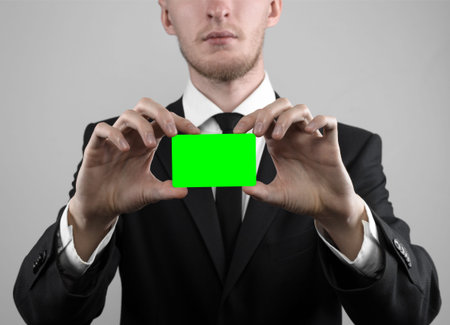 businessman in a black suit and black tie holding a card, a hand holding a card, green card, card is...