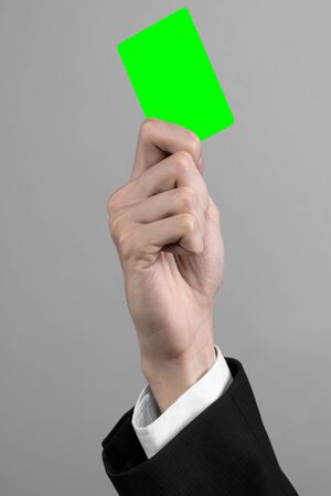 businessman in a black suit and black tie holding a card, a hand holding a card, green card, card is inserted, the green chroma key card, gray background, isolated, business theme, theme of bankingの写真素材