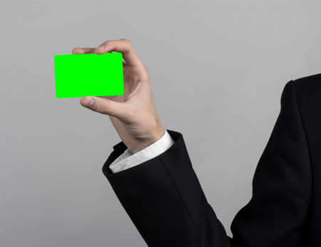 businessman in a black suit and black tie holding a card, a hand holding a card, green card, card is...