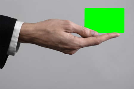 businessman in a black suit and black tie holding a card, a hand holding a card, green card, card is inserted, the green chroma key card, gray background, isolated, business theme, theme of bankingの写真素材