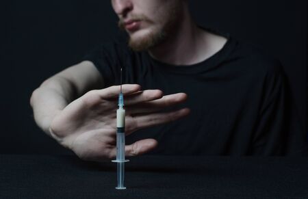 Addiction topic: addict holding syringe on a dark background studioの写真素材
