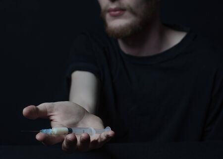 Addiction topic: addict holding syringe on a dark background studioの写真素材