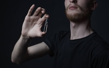 Addiction topic: addict holds a vial of a drug on a dark background studioの写真素材