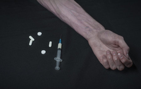 Addiction theme: hand addict with syringe with drugs on a dark background studio
