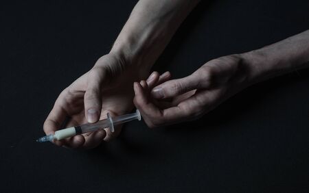 Addiction theme: hand addict with syringe with drugs on a dark background studioの写真素材