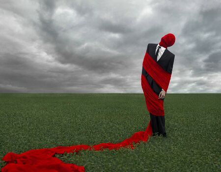 Man in a black suit with a red cloth is in the green field, loneliness, dreams, sleep, red fabric, storm clouds on the fieldの写真素材