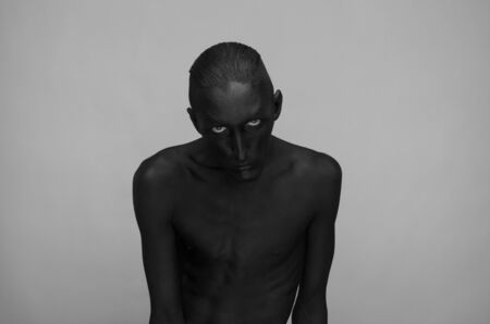 Gothic and Halloween theme: a man with black skin is isolated on a gray background in the studio, the Black Deathの写真素材