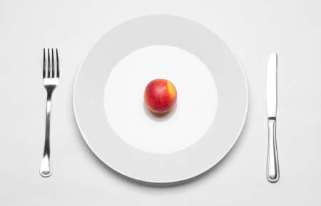Healthy eating in the restaurant and diet Topic: beautiful ripe nectarine on a white plate with a metal knife and fork lies on an isolated white table in studio top view studioの写真素材