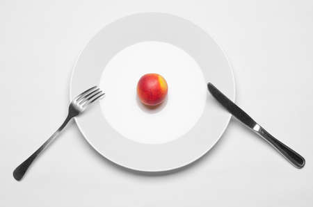 Healthy eating in the restaurant and diet Topic: beautiful ripe nectarine on a white plate with a metal knife and fork lies on an isolated white table in studio top view studioの写真素材