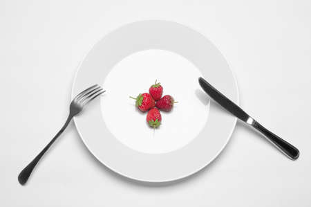 Healthy eating in the restaurant and diet Topic: white plate with three strawberries and a metal knife and fork lying on a white table in the studio isolated top viewの写真素材
