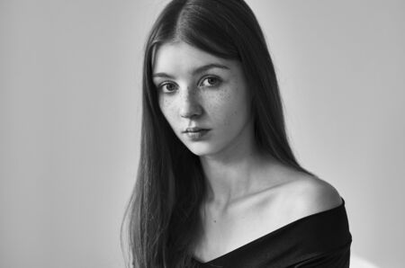 Dramatic black and white portrait of a beautiful lonely girl with freckles isolated on a white background in studioの写真素材
