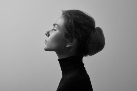 Dramatic black and white portrait of young beautiful girl with freckles in a black turtleneck on white background in studio shotの写真素材