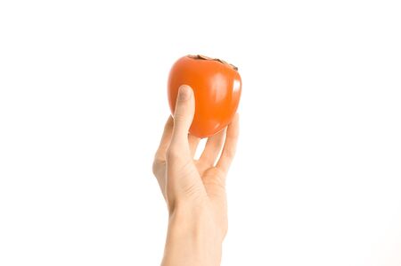 Healthy eating and diet Topic: Human hand holding a ripe persimmon isolated on a white background in the studio, first-person view shotの写真素材