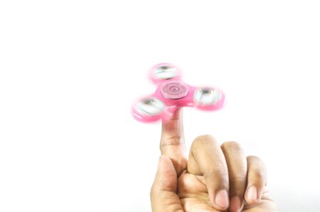 Pink colour fidget spinner holding on a finger tip and moving by a hand isolated in whiteの写真素材