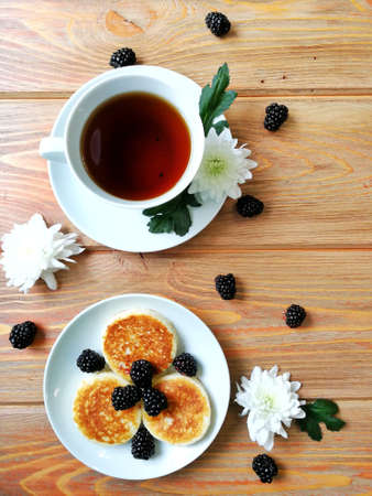BlackBerry and pancake on aged wooden background with flowers and coffeeの写真素材