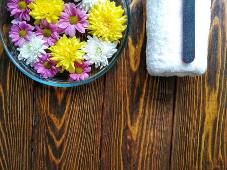 Spa manicure with a tray of flowers on a wooden background and a white fluffy towelの写真素材