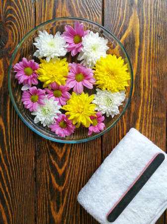 Spa manicure with a tray of flowers on a wooden background and a white fluffy towelの写真素材