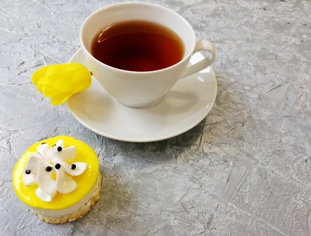 yellow Tulip with a Cup of tea on a grey textured background with cakeの写真素材