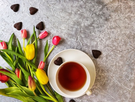 multi-colored tulips with a Cup of tea on a grey textured background with cakes and chocolatesの写真素材