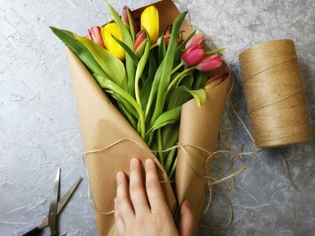 packaging of bouquet tulips Kraft paper on grey background with female handsの写真素材
