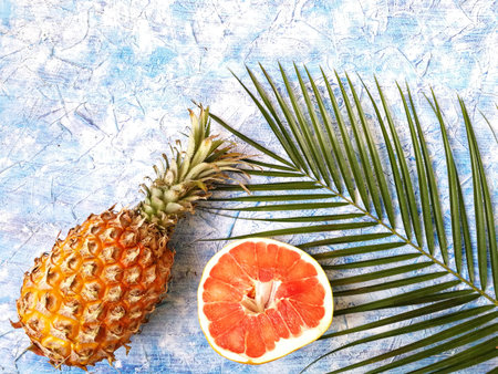pineapple, grapefruit and bananas with green palm tree branch on blue background
