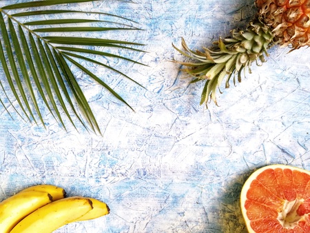 pineapple, grapefruit and bananas with green palm tree branch on blue backgroundの写真素材
