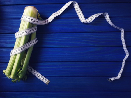 celery wrapped with measuring tape on blue backgroundの写真素材