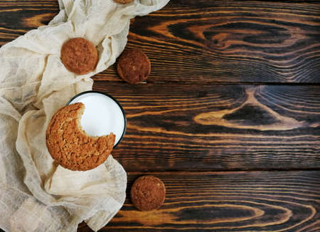 bitten oatmeal cookie with a glass of milk on a wooden table and runnerの写真素材