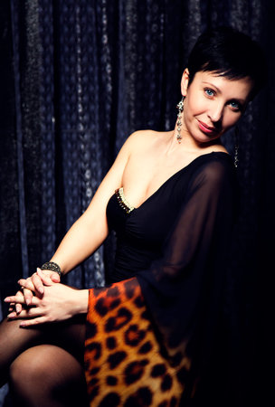 portrait of young brunette woman with short hair and holiday makeup in a black evening dress with...